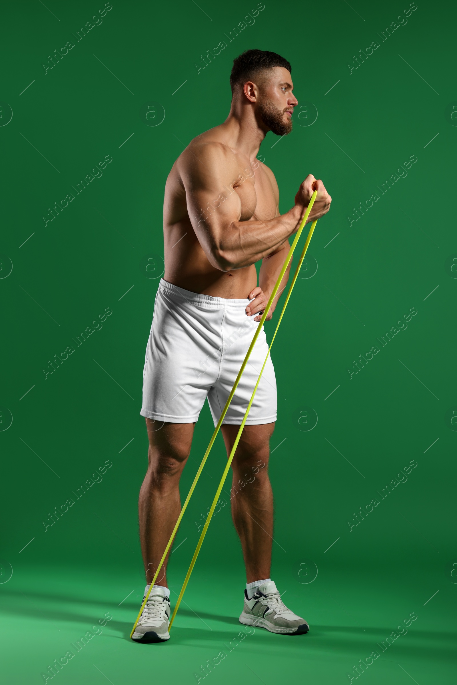 Photo of Muscular man exercising with elastic resistance band on green background