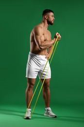 Muscular man exercising with elastic resistance band on green background