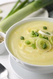 Bowl of tasty cream soup with leek on white table, closeup