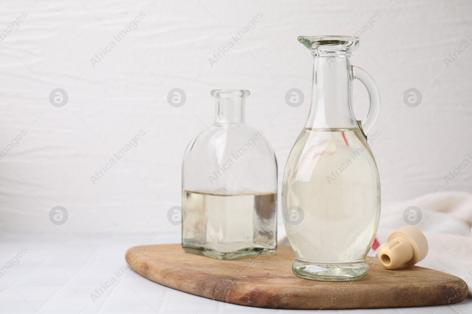 Photo of Vinegar in glass jug and bottle on white table, space for text