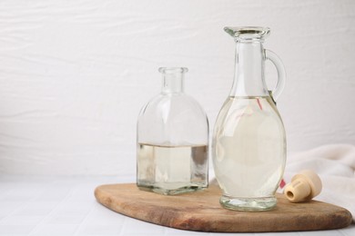 Vinegar in glass jug and bottle on white table, space for text