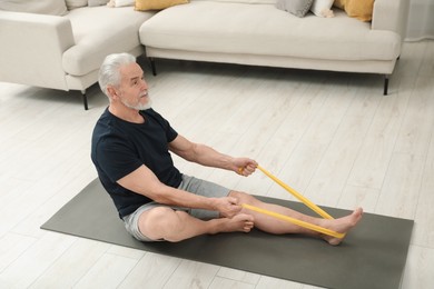 Senior man doing exercise with fitness elastic band on mat at home