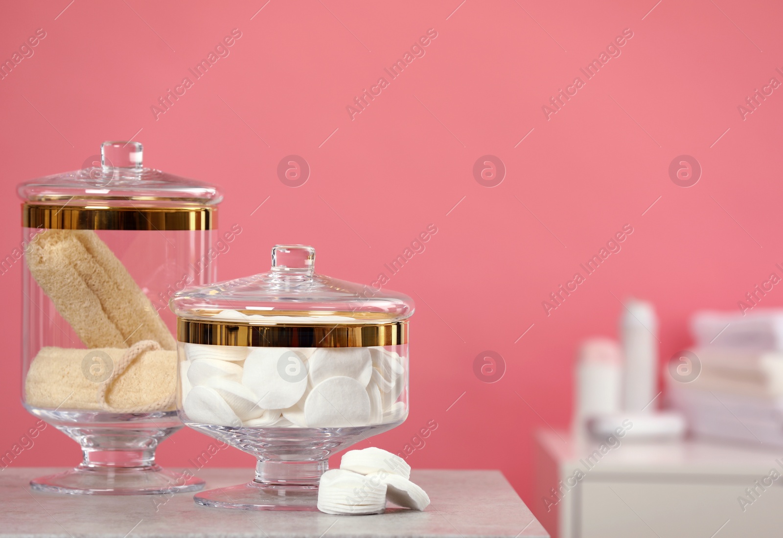 Photo of Composition of glass jars with cotton pads on table against pink background. Space for text