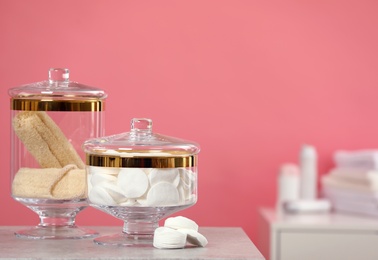 Composition of glass jars with cotton pads on table against pink background. Space for text