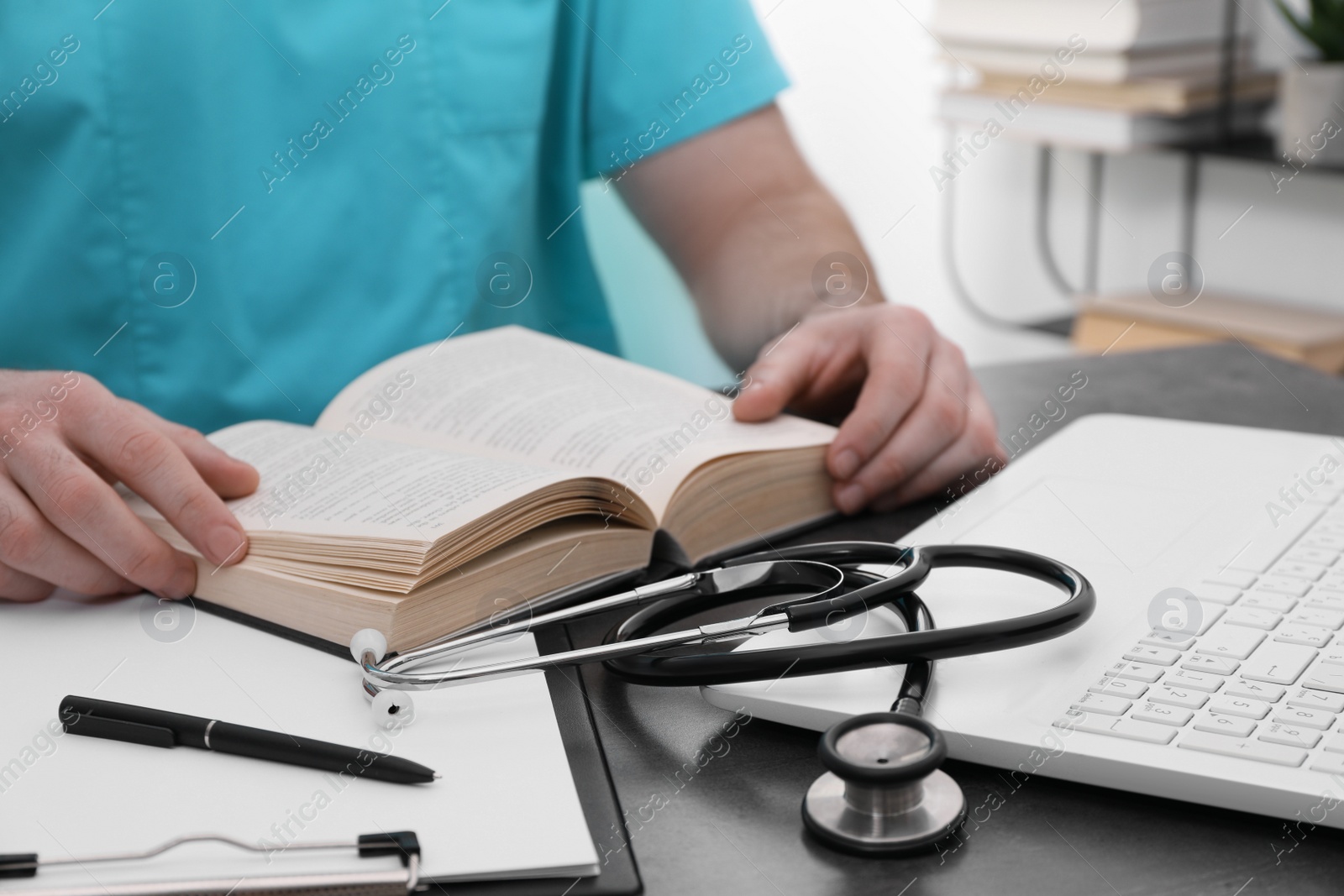 Photo of Medical student in uniform studying at table indoors, closeup