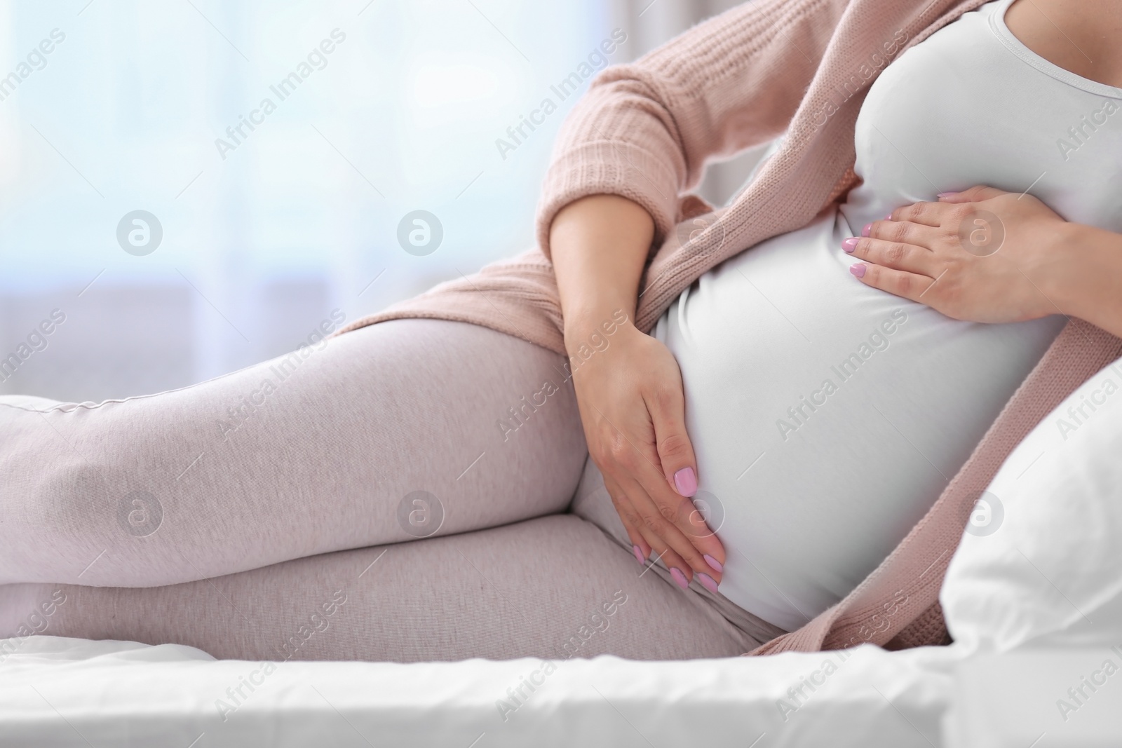 Photo of Young pregnant woman lying on bed and touching her belly at home, closeup