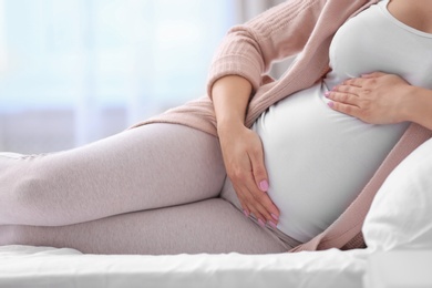 Young pregnant woman lying on bed and touching her belly at home, closeup