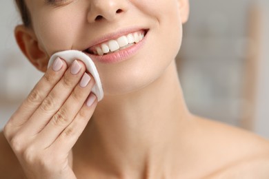 Photo of Smiling woman removing makeup with cotton pad on blurred background, closeup