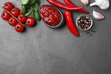 Photo of Flat lay composition with bowl of chili sauce and ingredients on grey table. Space for text