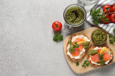 Photo of Delicious bruschettas with cream cheese, salmon and pesto sauce on light grey table, flat lay. Space for text