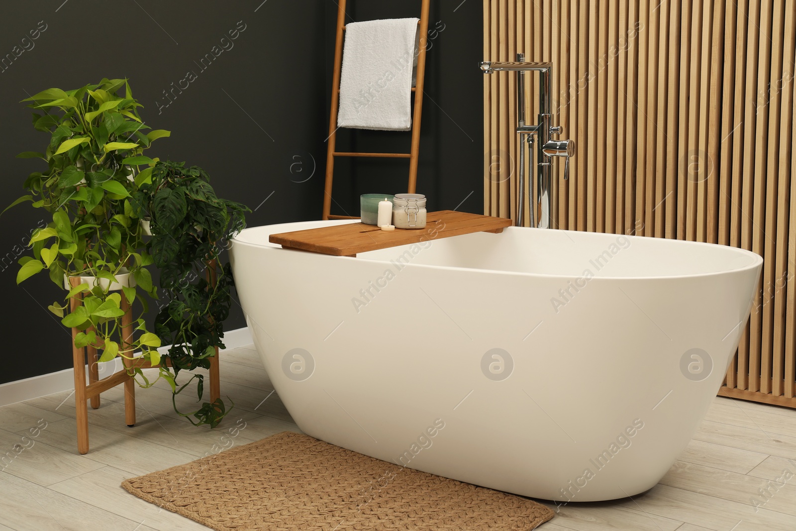 Photo of Spa day. Ceramic tub with wooden tray and green houseplants in bathroom