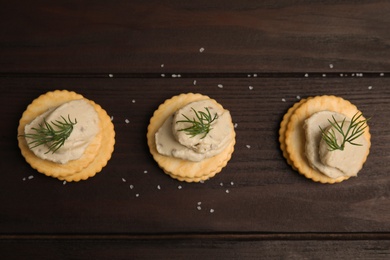 Photo of Delicious crackers with humus and dill on wooden table, flat lay