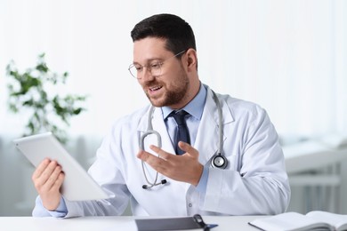 Smiling doctor having online consultation via tablet at table in clinic