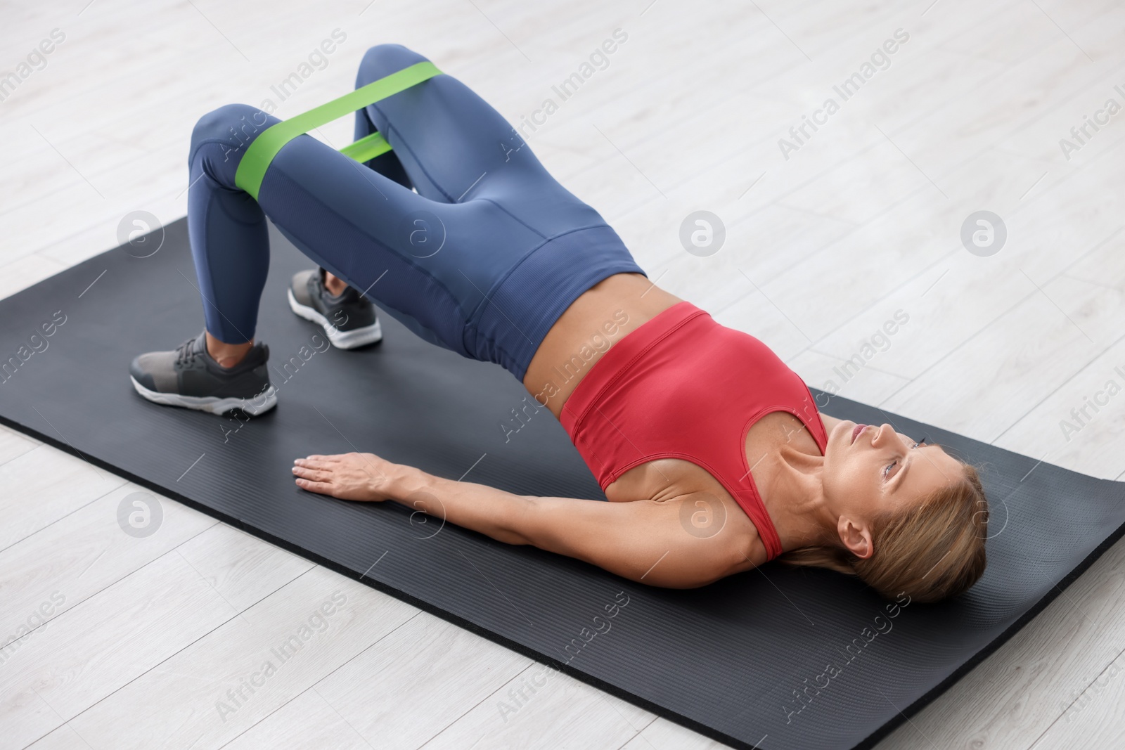 Photo of Athletic woman doing exercise with fitness elastic band on mat indoors