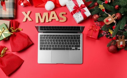 Flat lay composition with laptop, gift boxes and Christmas decor on red background