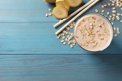 Photo of Glass of tasty banana smoothie with oatmeal on light blue wooden table, flat lay. Space for text