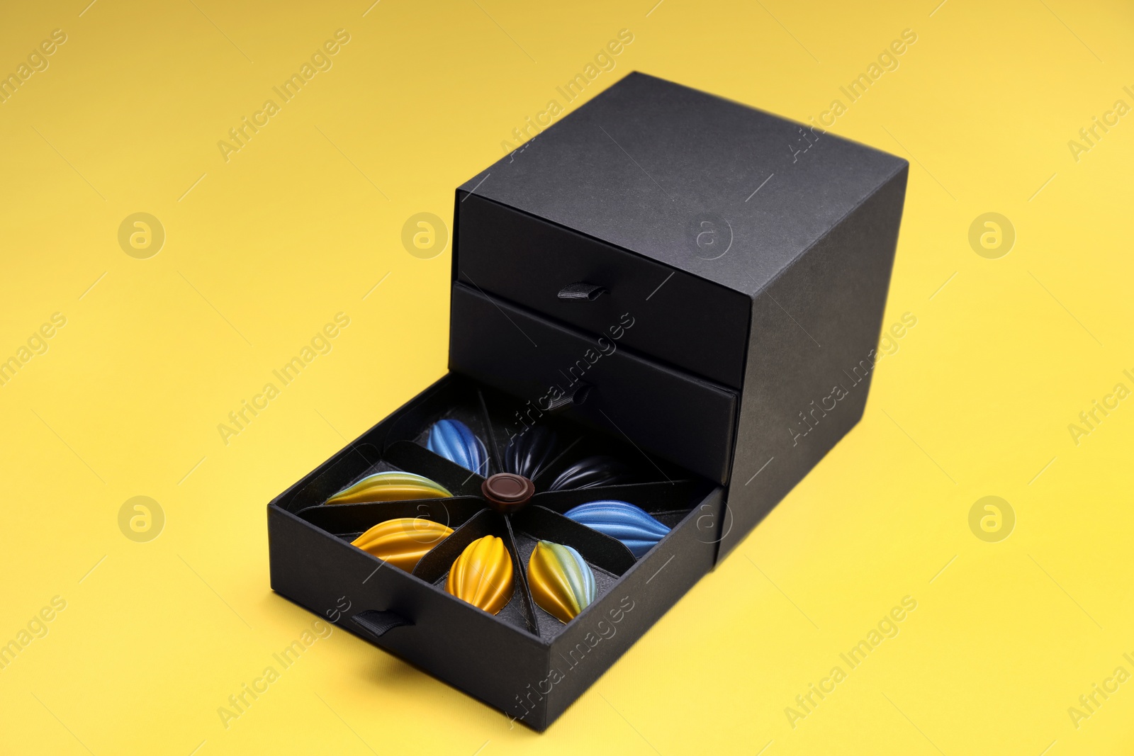 Photo of Box of tasty chocolate candies on yellow background