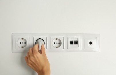 Woman putting plug into socket indoors, closeup