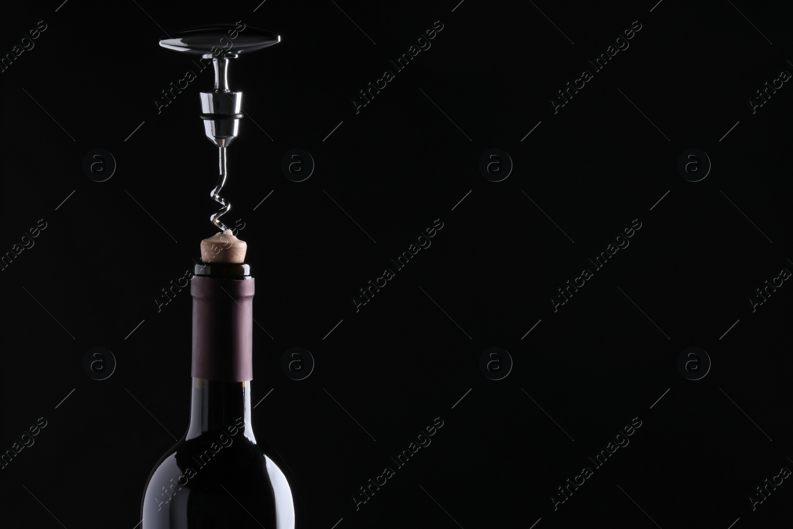 Photo of Opening wine bottle with corkscrew on dark background, closeup. Space for text