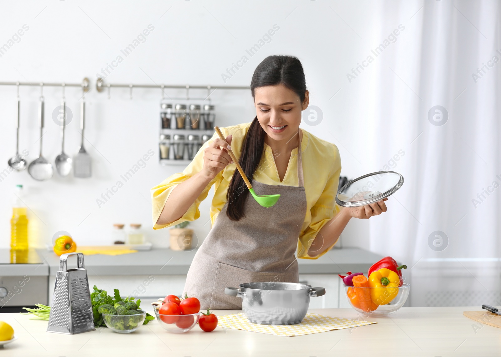 Photo of Young woman cooking tasty soup in kitchen