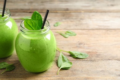 Photo of Jars of healthy green smoothie with fresh spinach on wooden table. Space for text