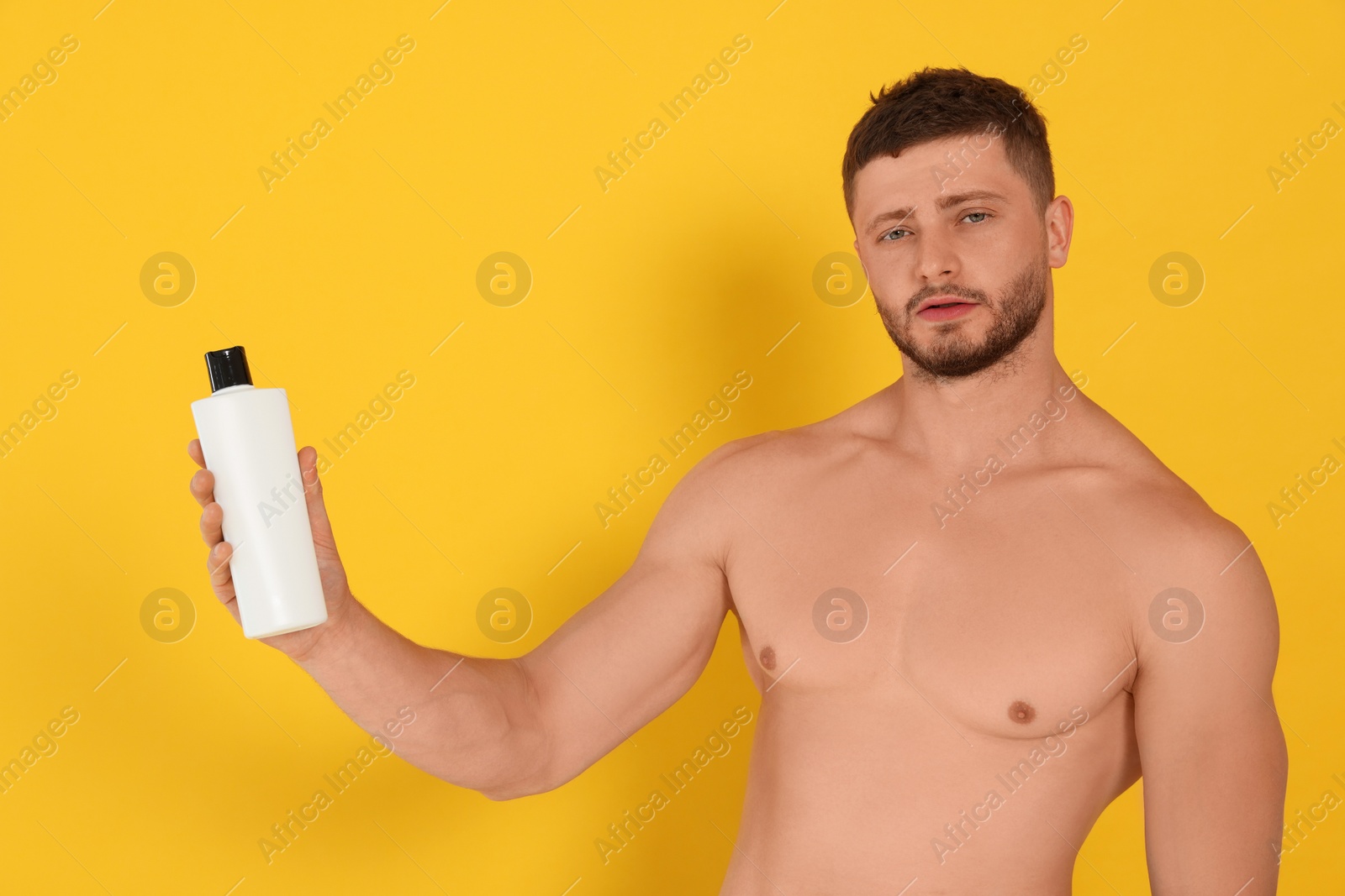 Photo of Shirtless young man holding bottle of shampoo on orange background