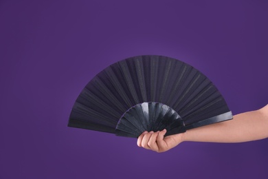 Photo of Woman holding black hand fan on purple background, closeup