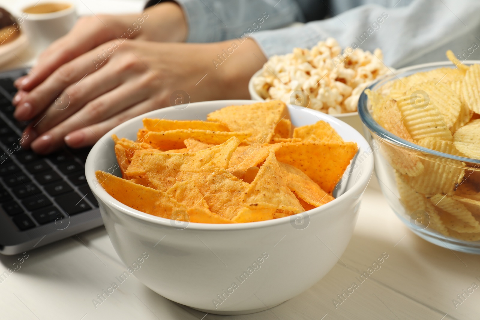 Photo of Bad eating habits. Woman working on laptop at white wooden table with different snacks, selective focus