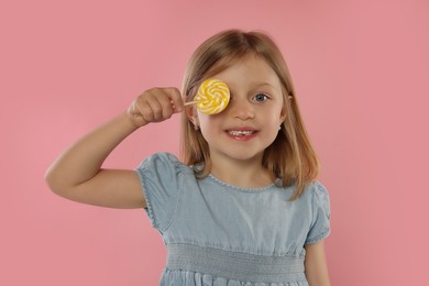 Happy girl covering eye with lollipop on pink background