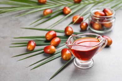 Photo of Palm oil in glass jug, tropical leaves and fruits on grey table. Space for text