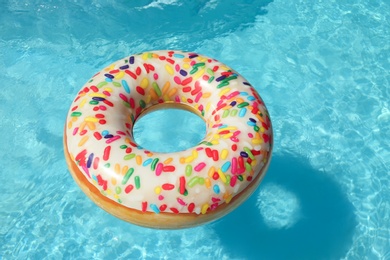 Bright inflatable doughnut ring floating in swimming pool on sunny day