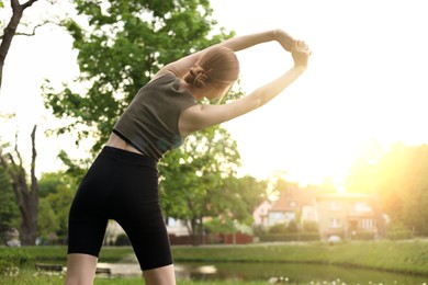 Woman doing morning exercise in park, back view. Space for text