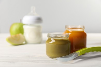 Photo of Jars with healthy baby food and spoon on white wooden table. Space for text