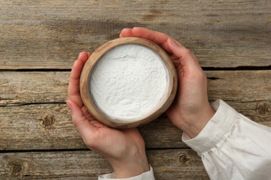 Photo of Woman holding bowl with baking powder at wooden table, top view