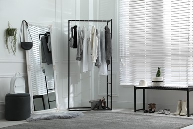 Rack with stylish women's clothes and large mirror in dressing room. Interior design