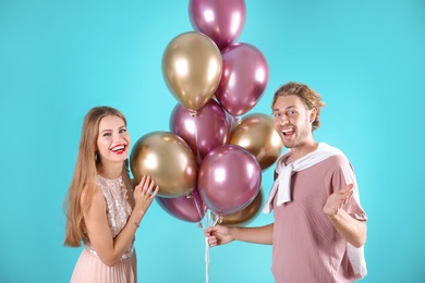 Young couple with air balloons on color background