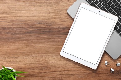 Modern tablet, laptop, houseplant and clips on wooden table, flat lay. Space for text