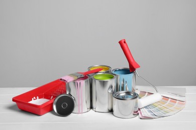 Photo of Cans of paints, roller, tray and palette on white wooden table