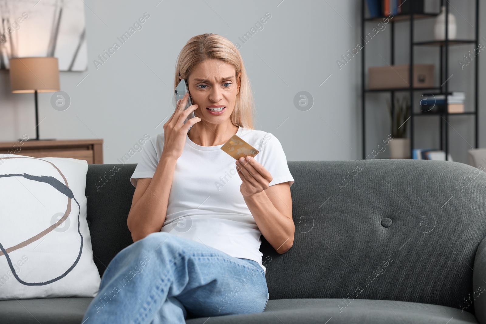 Photo of Stressed woman with credit card talking on smartphone at home, space for text. Be careful - fraud