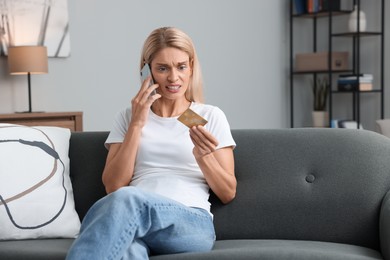 Stressed woman with credit card talking on smartphone at home, space for text. Be careful - fraud