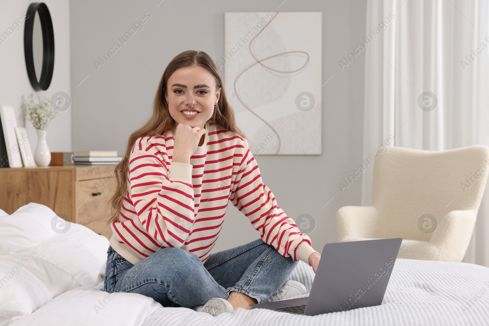 Photo of Happy woman with laptop on bed in bedroom