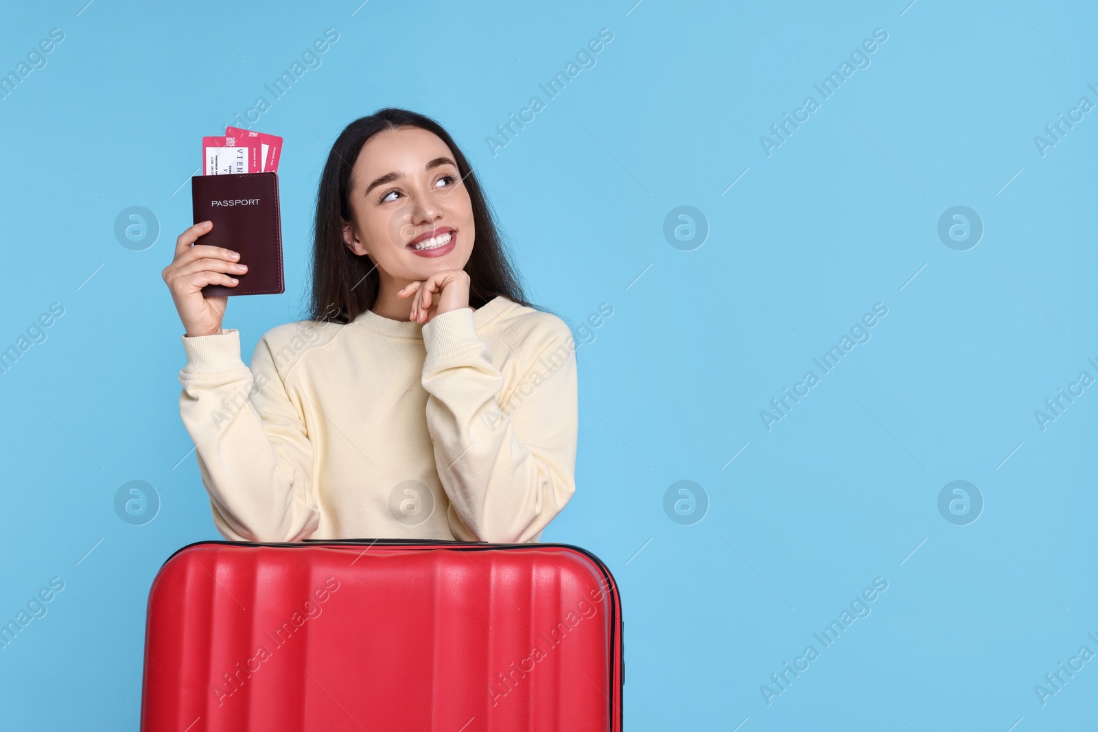 Photo of Smiling woman with passport, tickets and suitcase on light blue background. Space for text