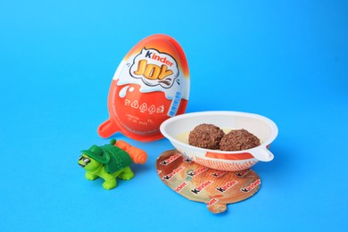 Photo of Slynchev Bryag, Bulgaria - May 25, 2023: Kinder Joy Egg with sweet candies and toy turtle on light blue background