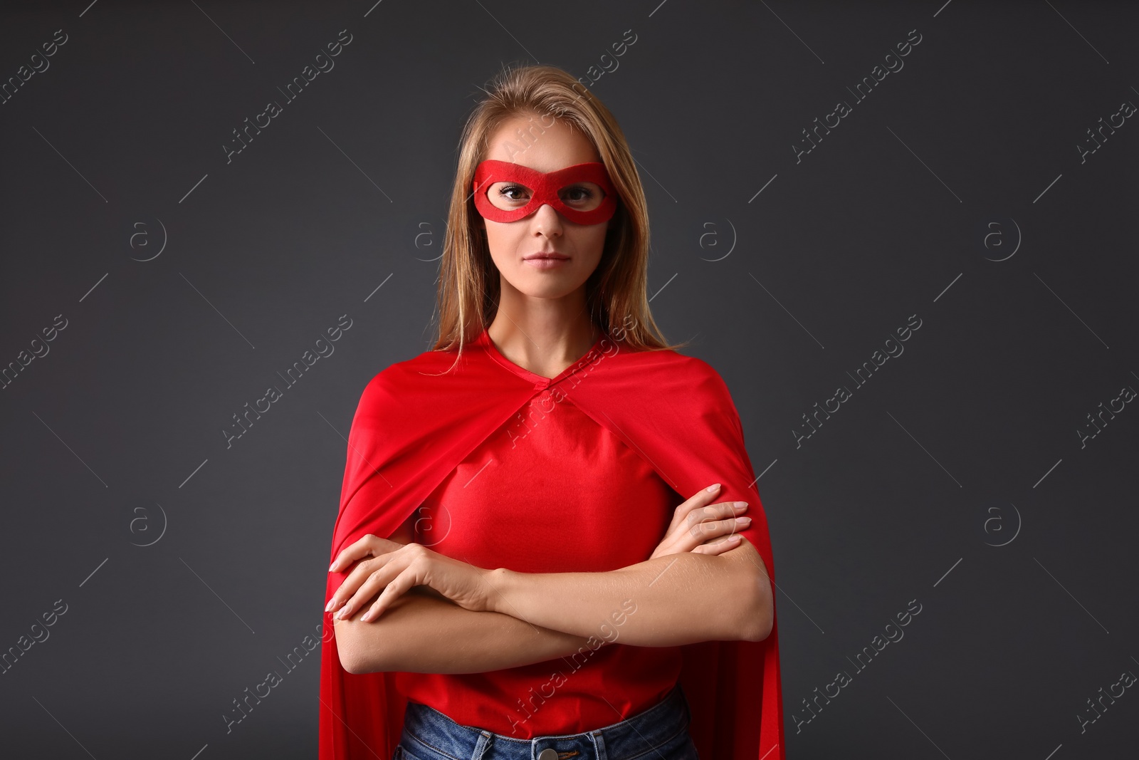 Photo of Confident woman wearing superhero cape and mask on grey background