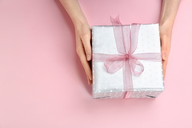 Photo of Young woman holding beautiful gift box on color background, top view