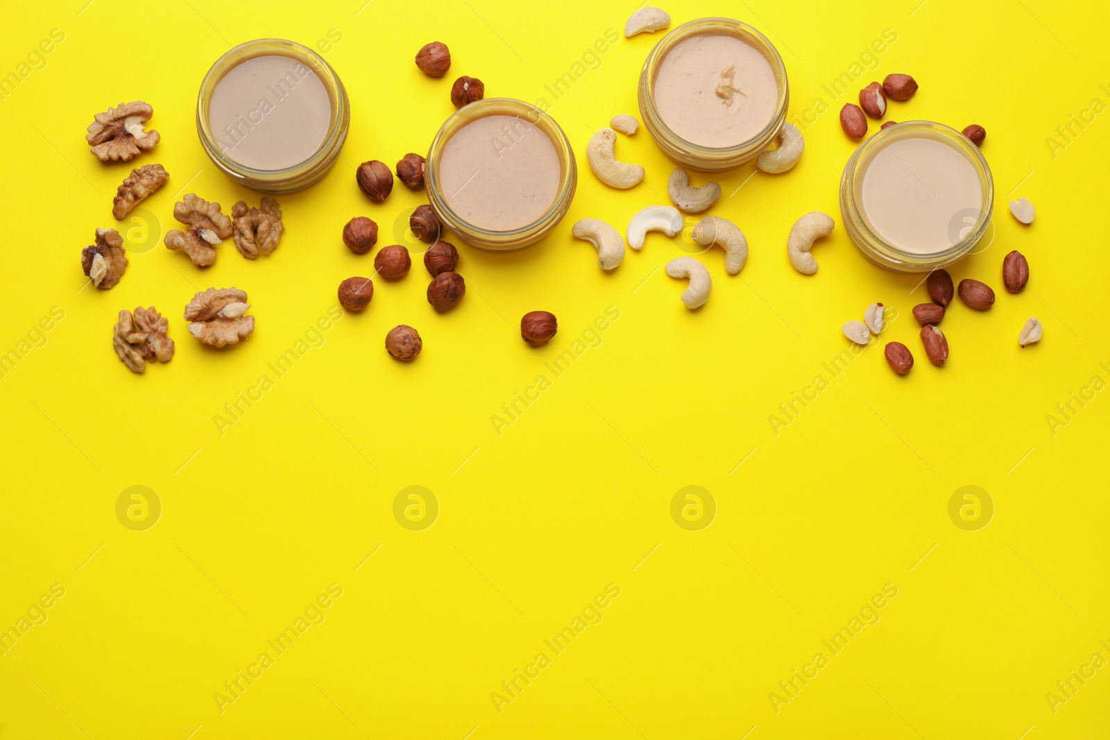 Photo of Different types of nut butter and ingredients on yellow background, flat lay. Space for text