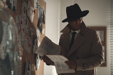 Detective with newspaper near evidence board in office
