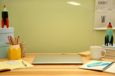 Photo of Stylish workplace with laptop and stationery on wooden desk near light green wall. Interior design