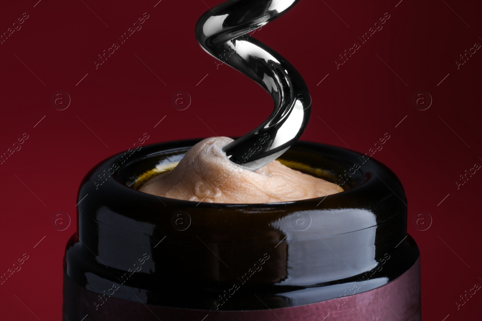 Photo of Opening bottle of wine with corkscrew on burgundy background, closeup