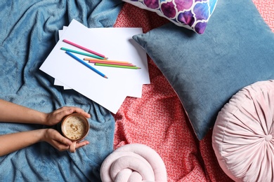 Photo of Woman holding cup of coffee while lying on bed with pillows and warm plaid, top view